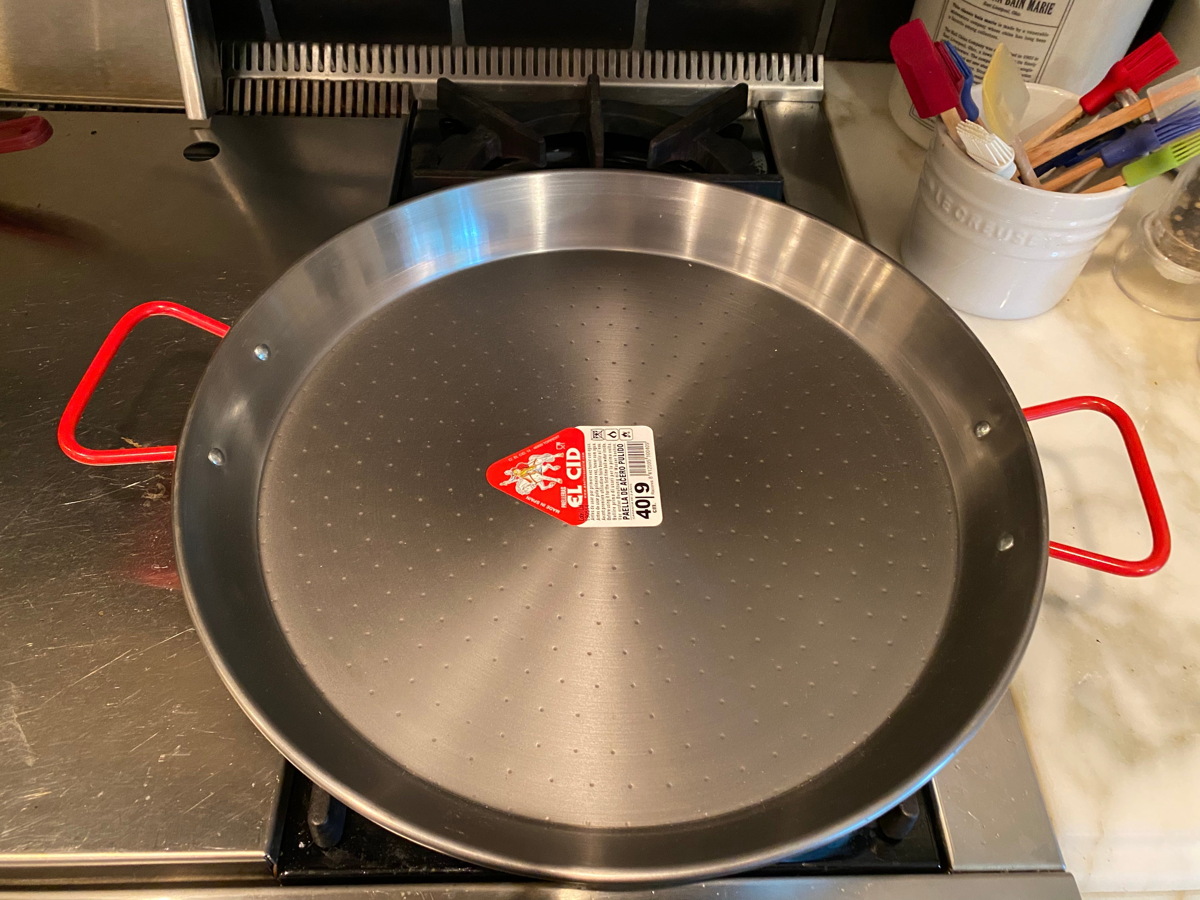 A traditional Spanish carbon steel paella pan being seasoned on a stovetop — care guide from ekuBOX Spanish Paella & Tapas Gift Box