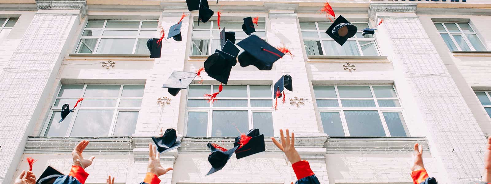 Raised arms and hands tossing graduation caps in the air, representing a graduation celebration and milestone gifting moment.