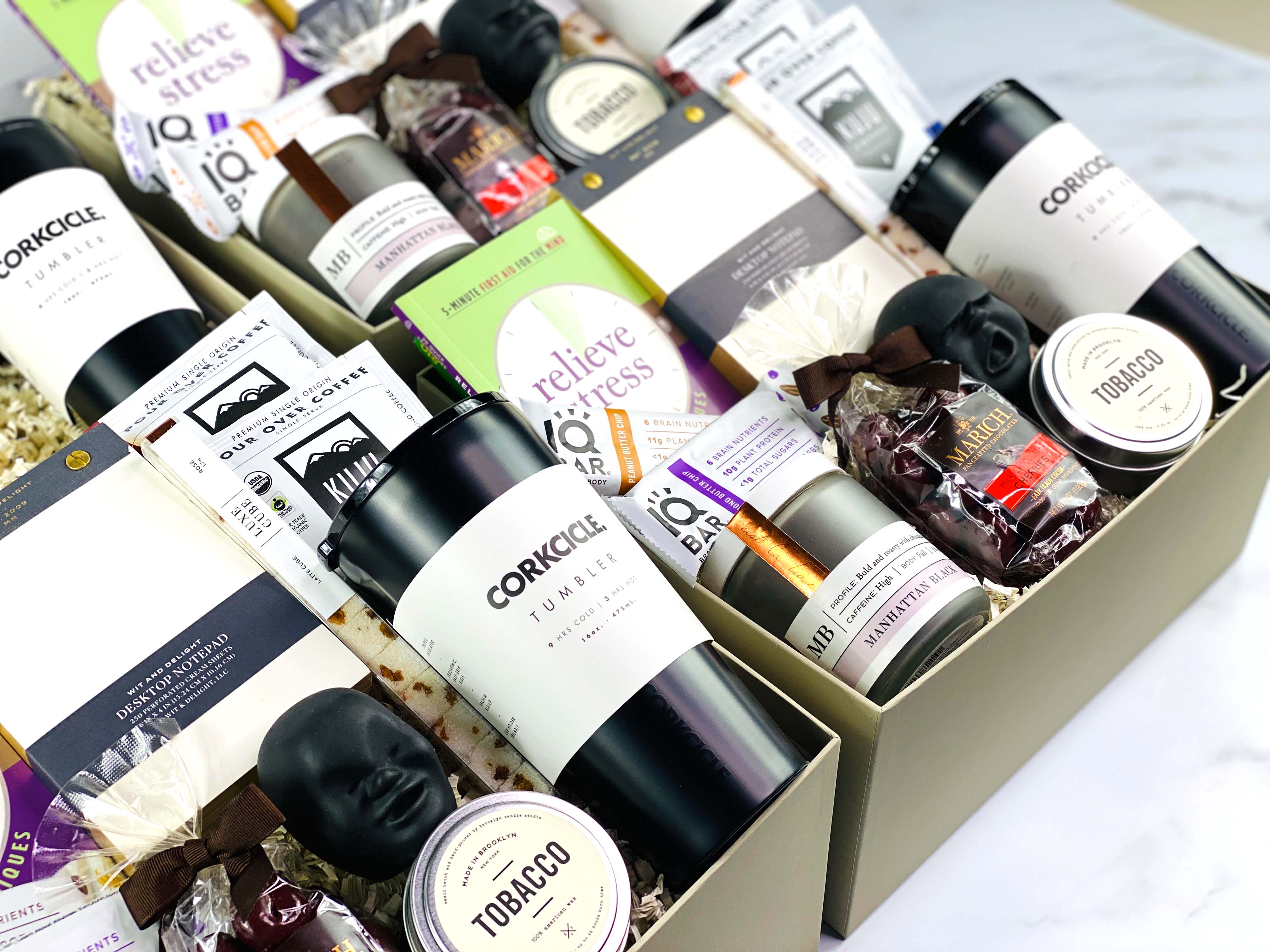 Corporate gift boxes arranged together, featuring gourmet snacks, a stress relief ball, a thermal beverage container, travel candle, and a luxury notebook for professional gifting.