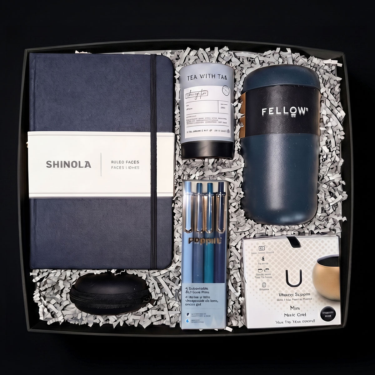 Gift box with Shinola notebook, Fellow tumbler, U Mini Speaker, Poppin Pens, Tea Tube, and 4 stress balls, on a marble surface.