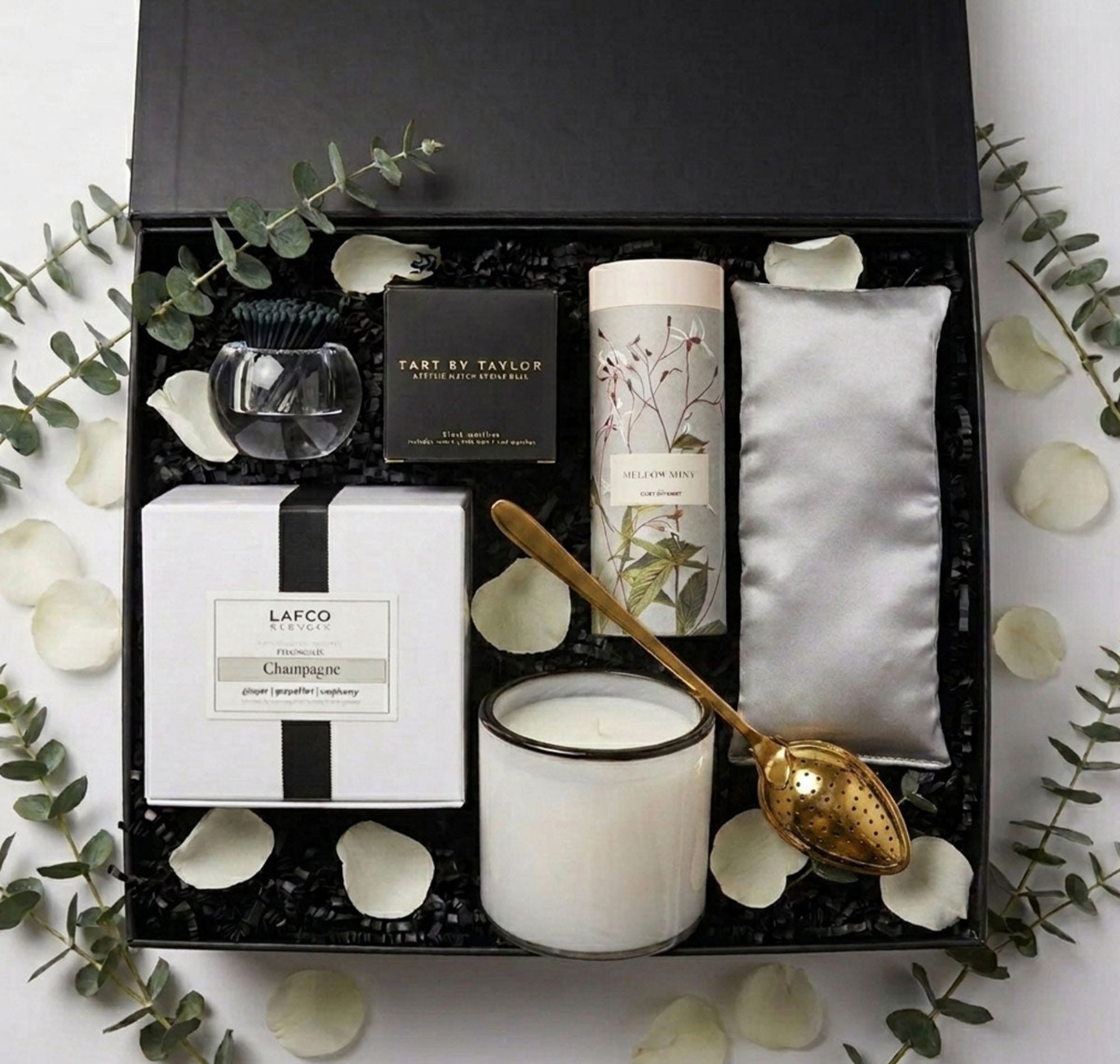 Modern Serenity spa set in a black box with a candle, a tube of tea and a gold spoon, tart by Taylor acrylic match holder and black matches and a silk eye pillow with rose petals and eucalyptus