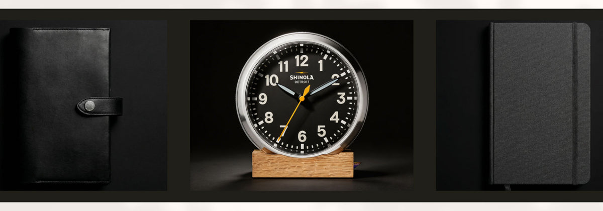 Shinola clock on a wooden stand with black leather cover and notebook in the background in the Shinola Collection