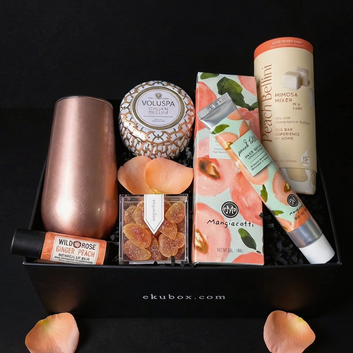 A luxury black ekubox gift set containing a rose gold thermal flute, a Voluspa Prosecco Bellini candle, Sugarfina gummies, Mangiacotti peach hand cream, Teaspressa bellini sugar cubes, and organic ginger peach lip balm, styled with peach rose petals.