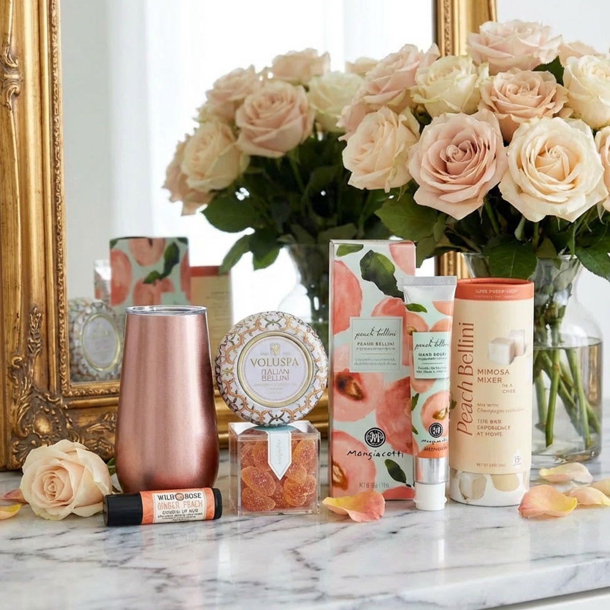 peach bellini candle, lip balm, hand cream and Teaspressa bellini sugar cubes on a marble table with roses and a mirror.