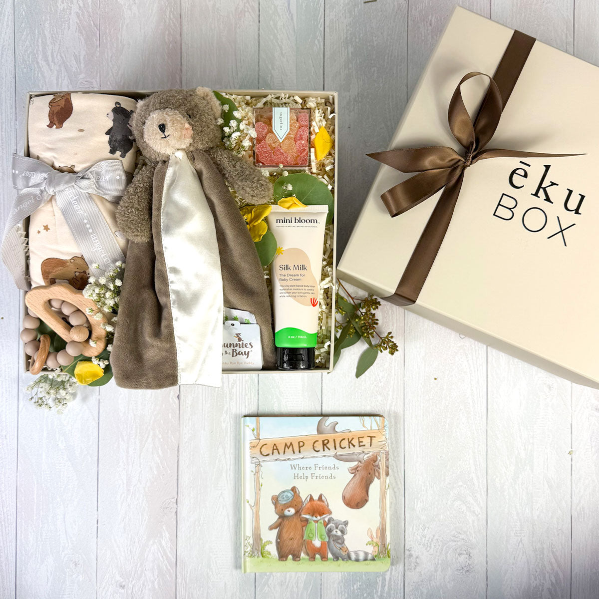 view of Baby Bear newborn gift box featuring a brown bear lovey, bear-print swaddle, silicone teether, baby cream, storybook, and Sugarfina gummy bears arranged in a gift box.