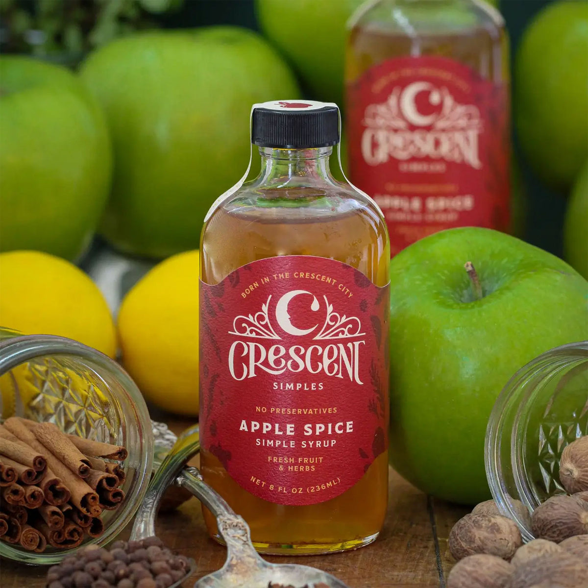 Crescent apple spice syrup on a wooden table with apples and nuts surrounding it
