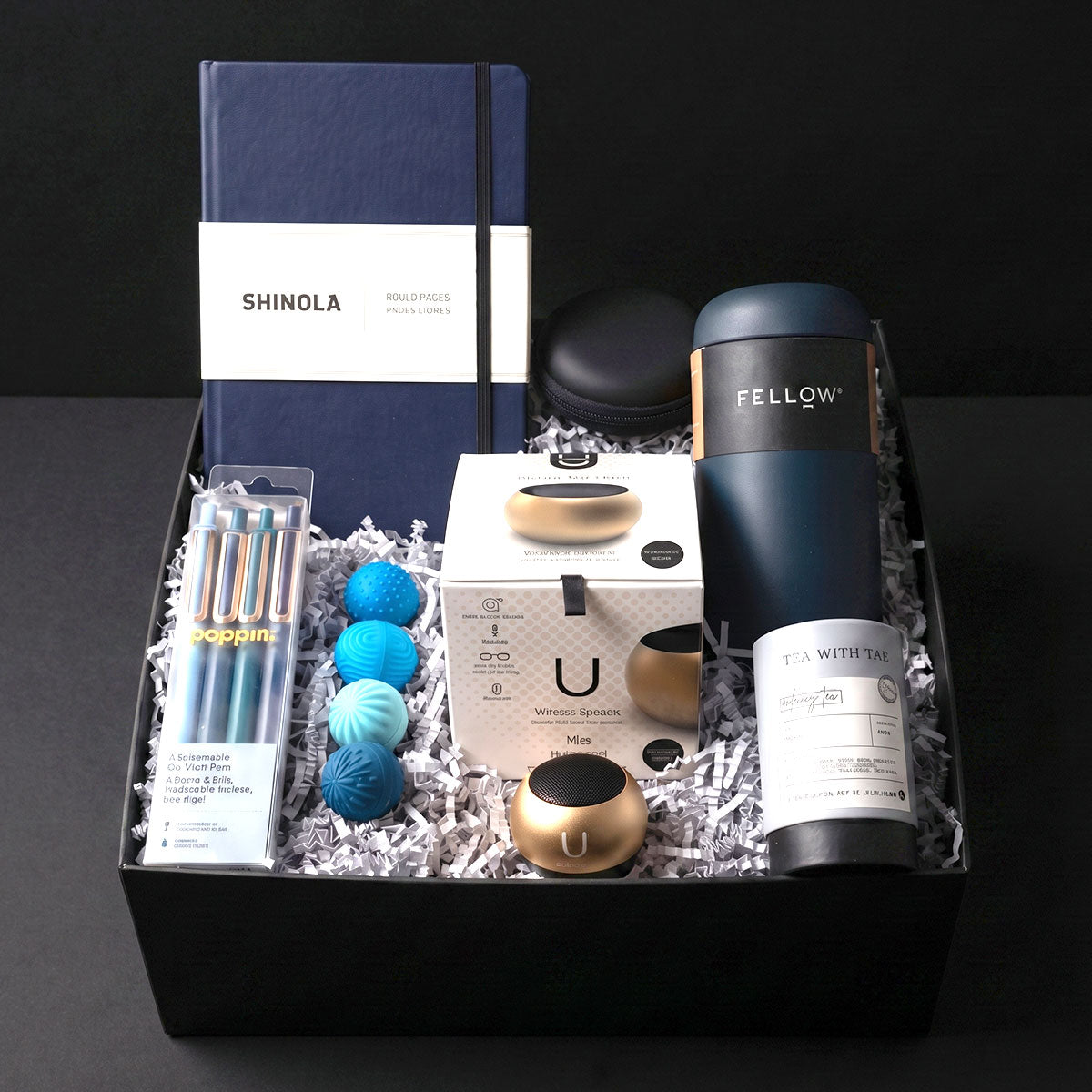 Gift box with Shinola notebook, Fellow tumbler, U Mini Speaker, Poppin Pens, Tea Tube, and 4 stress balls, on a marble surface.
