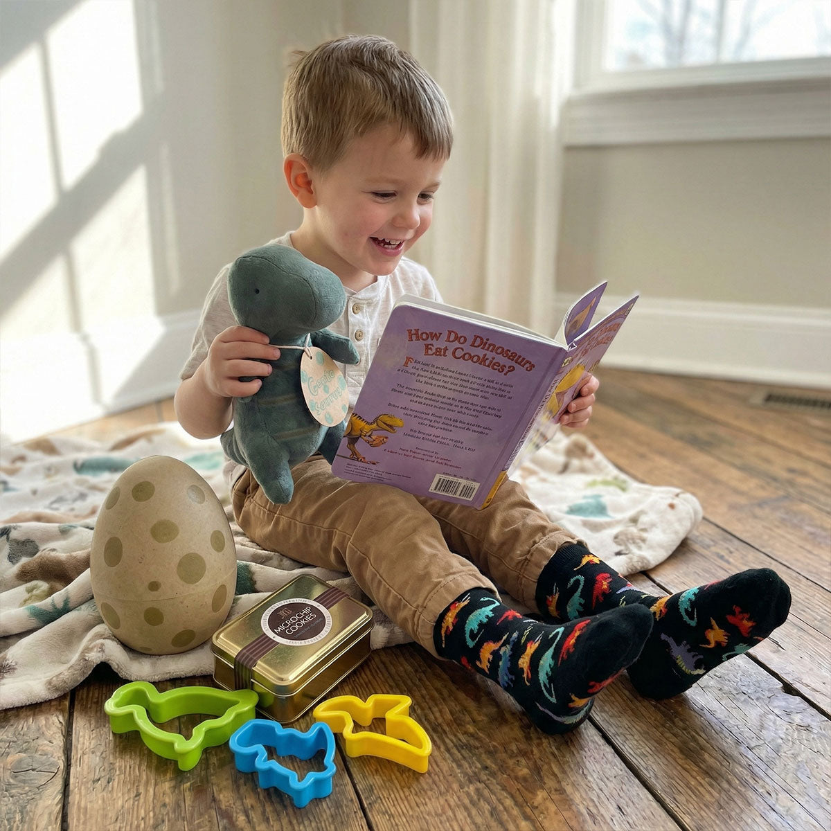Child reading a book with a toy Maileg dino on a wooden floor