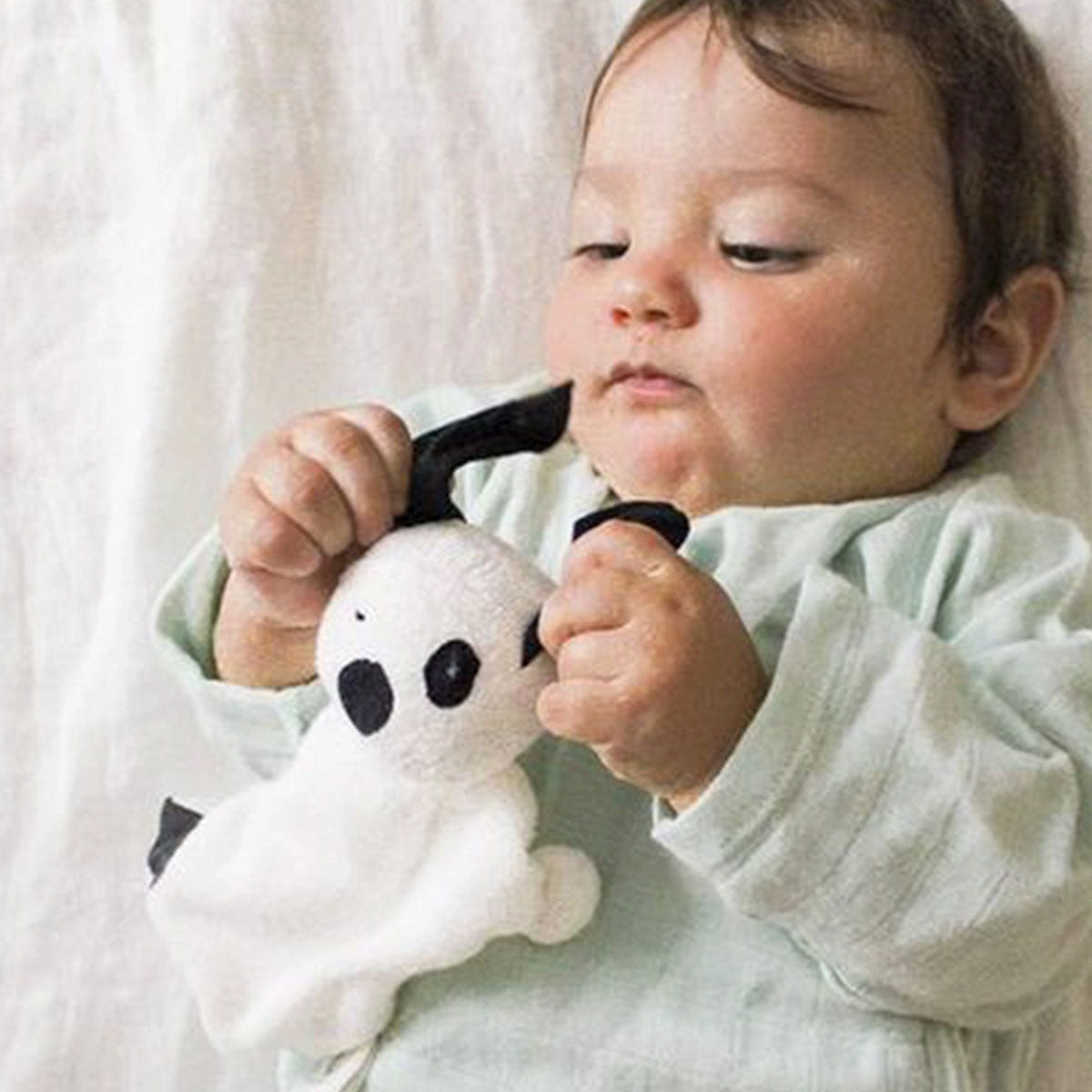 Baby holding a puppy lovey toy against a soft, neutral background