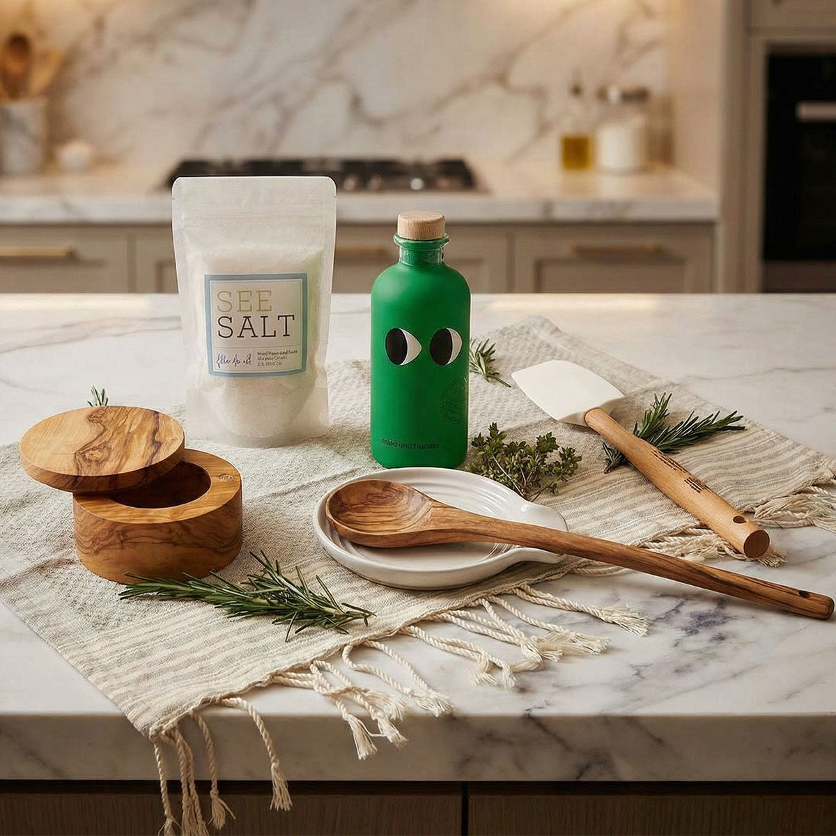 Kitchen counter with a bottle of olive oil, wooden spoon, and salt container on a marble countertop.