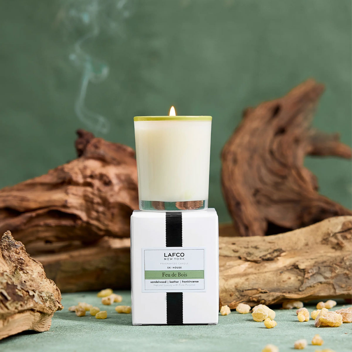 Lafco candle with packaging on a green background with wood and stones