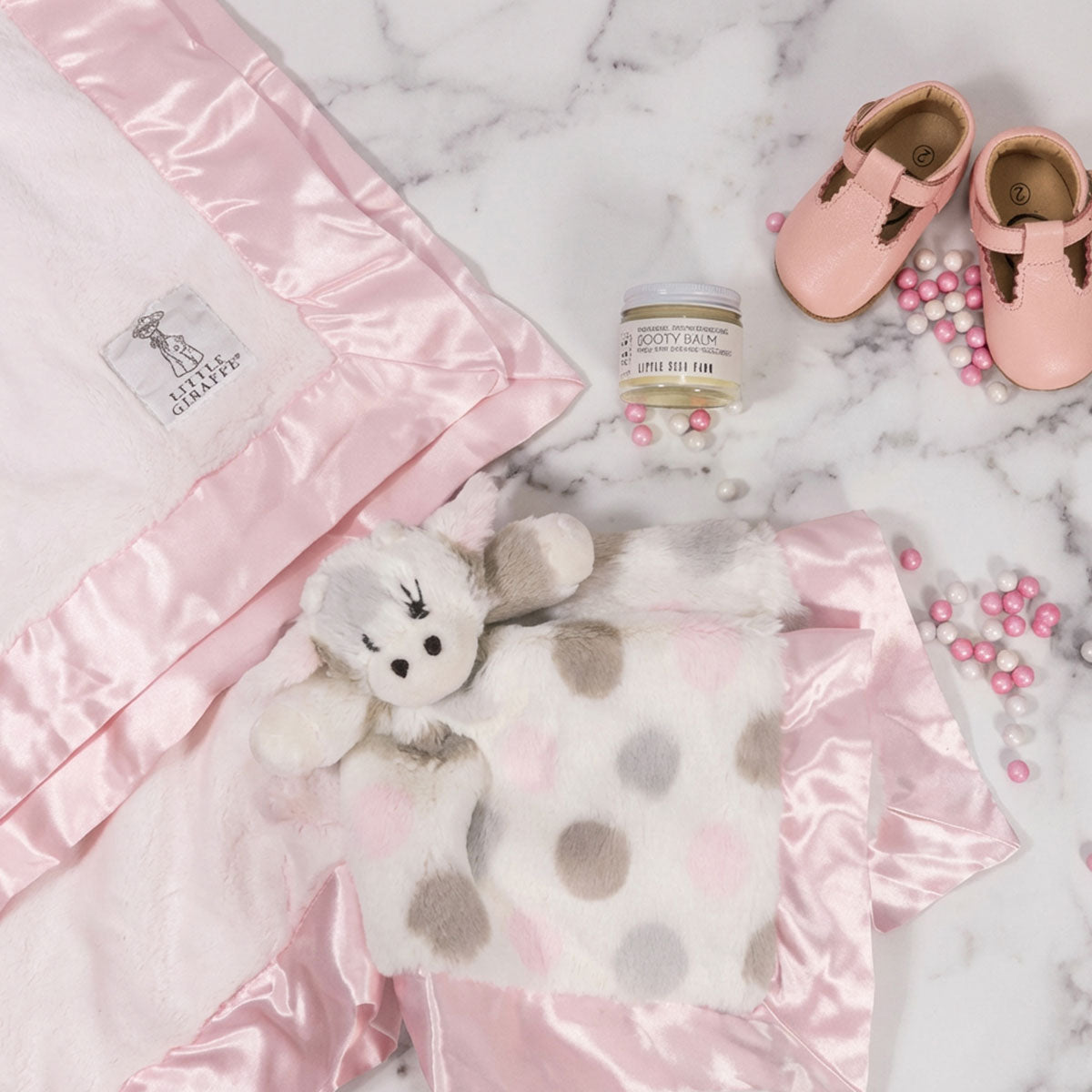 Newborn Baby gift box including a pink little giraffe blanket, teddy bear, shoes, on a marble surface