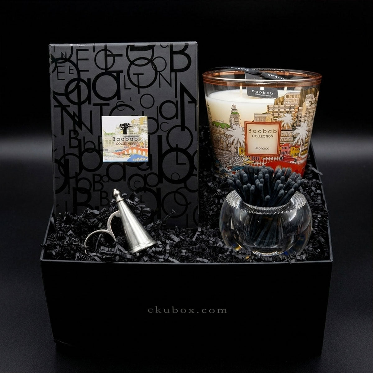 Gifting box with Baobab Monaco candle, the conacil snuffer, and an acrylic match container on a dark background