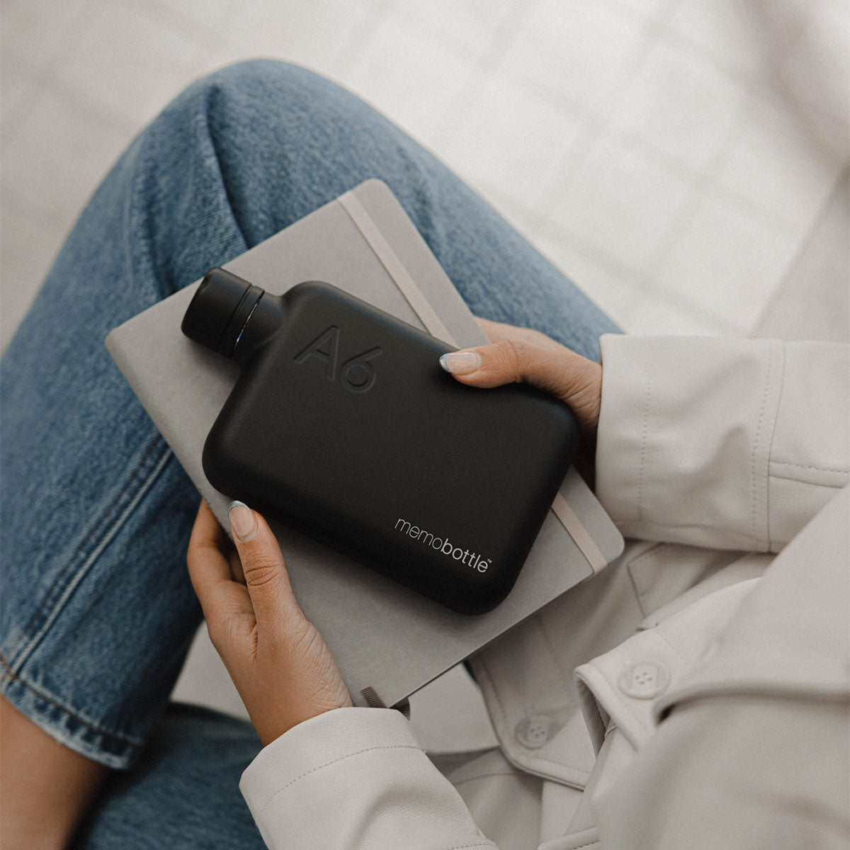 Person holding a black Membottle on a notebook with a light background