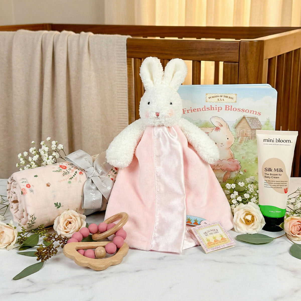 Baby girl gift box with a pink bunny lovey, floral swaddle, baby book, teether, and body cream in nursery