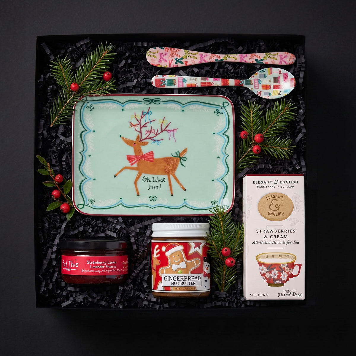 Oh What Fun Gift in a black gift box with a small holiday tray, a colorful spreader and spoon with a jar of strawberry jam, gingerbread nut butter and a box of strawberry and cream cookies.