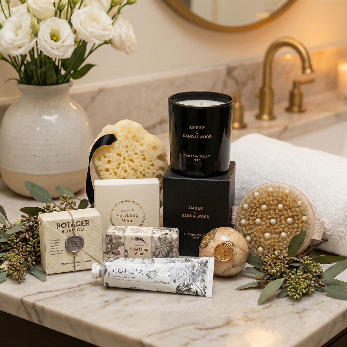 Bathroom counter with soap, candle, and bath products with a vase of flowers and towel in the background.