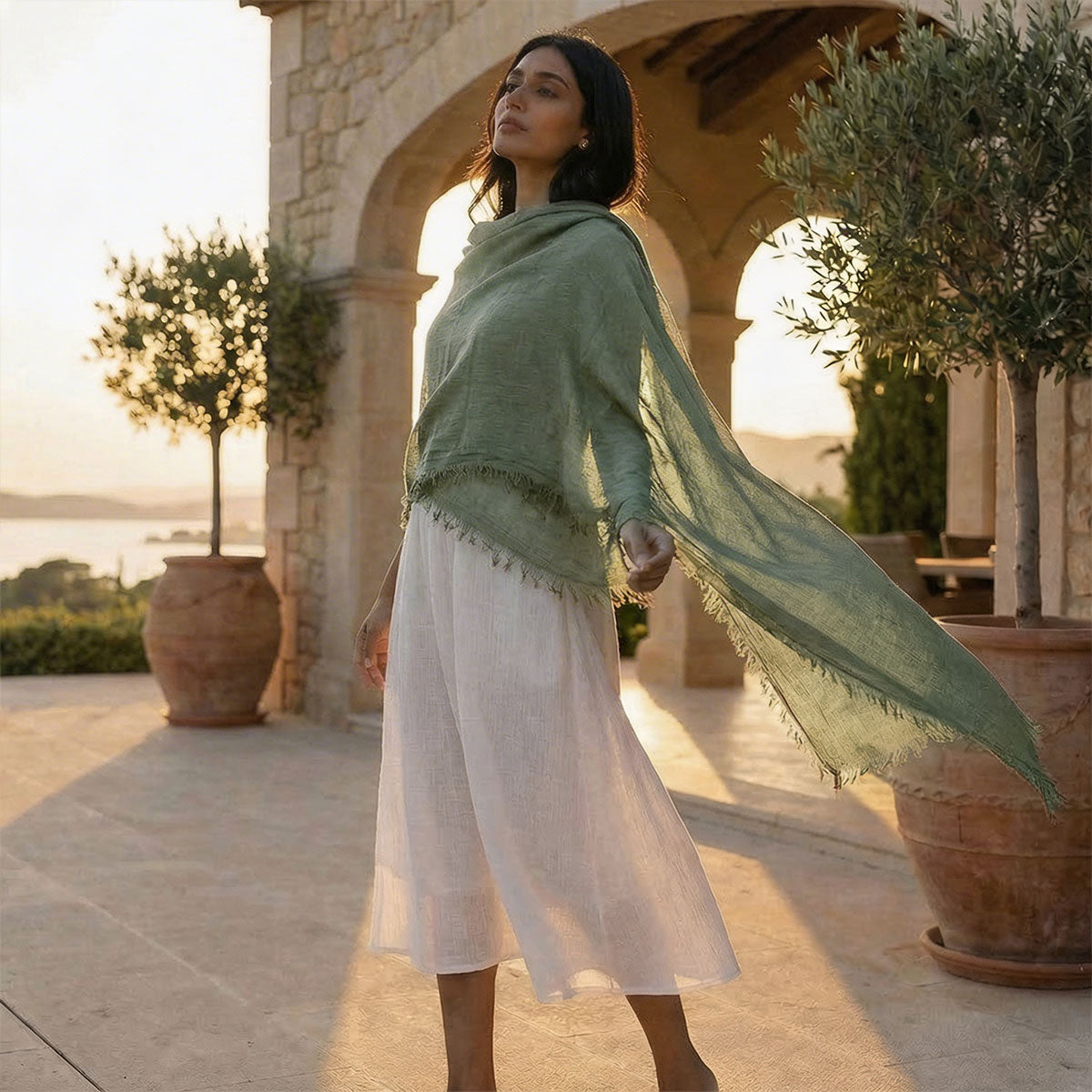 Woman in a boho scarf and white dress standing in a sunlit outdoor setting.