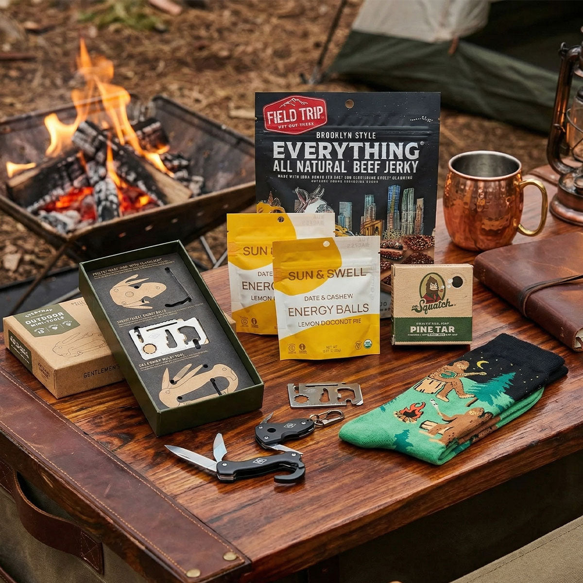 Outdoor setting with pine soap, socks, jerky and survial tools, snacks, and a fire pit in the background.