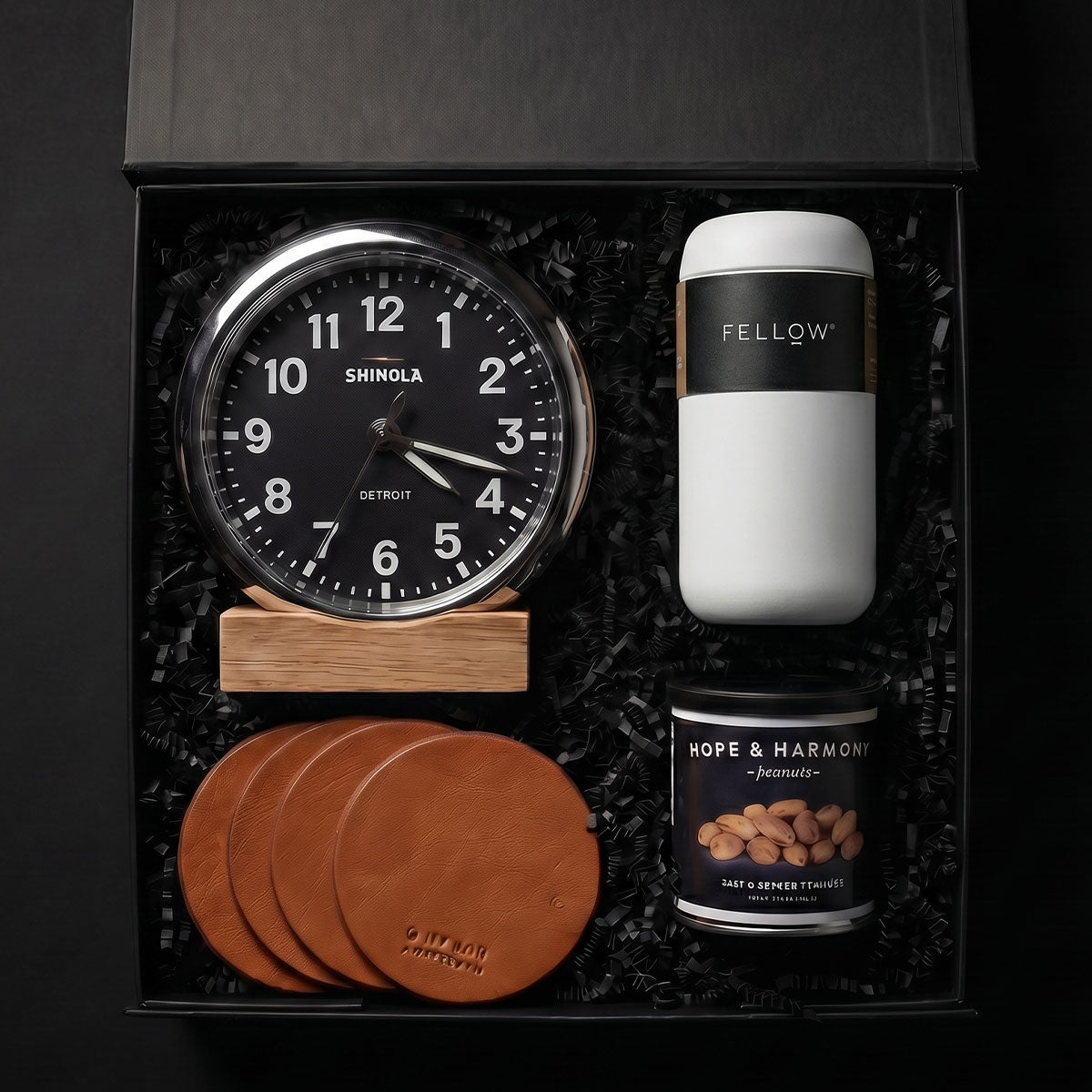Gift set with Shinola Runwell clock in black, Fellow coffee container, leather coaster set, and Hope & Harmony peanuts in a box.