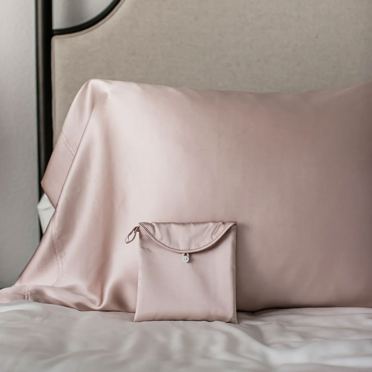 Folded pink satin pillowcase on a bed with a pillow in the background