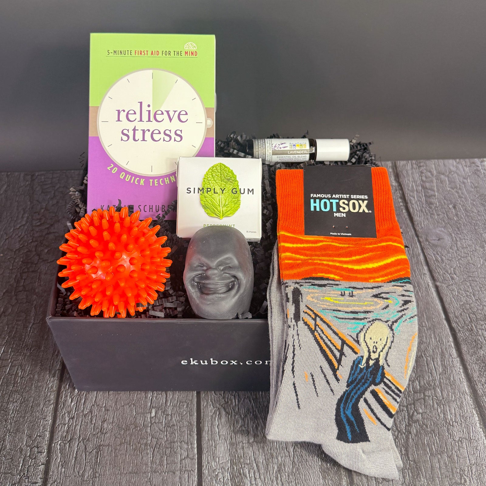 A gift box containing various items to relieve stress, including a stress ball, lavender oil roller, gum, a book, and a pair of socks .