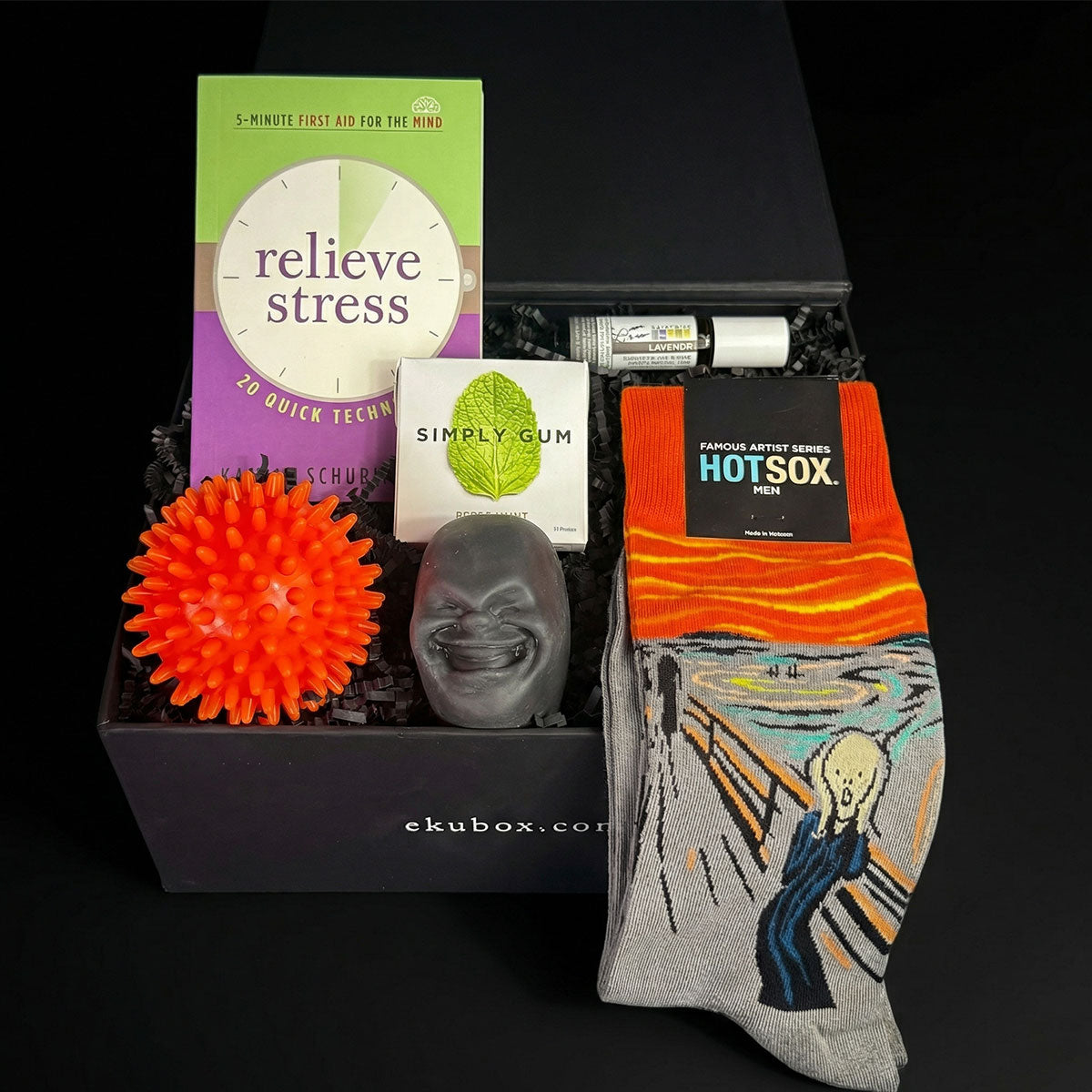 Gift box with stress relief items including a book, socks, and stress ball on a black background