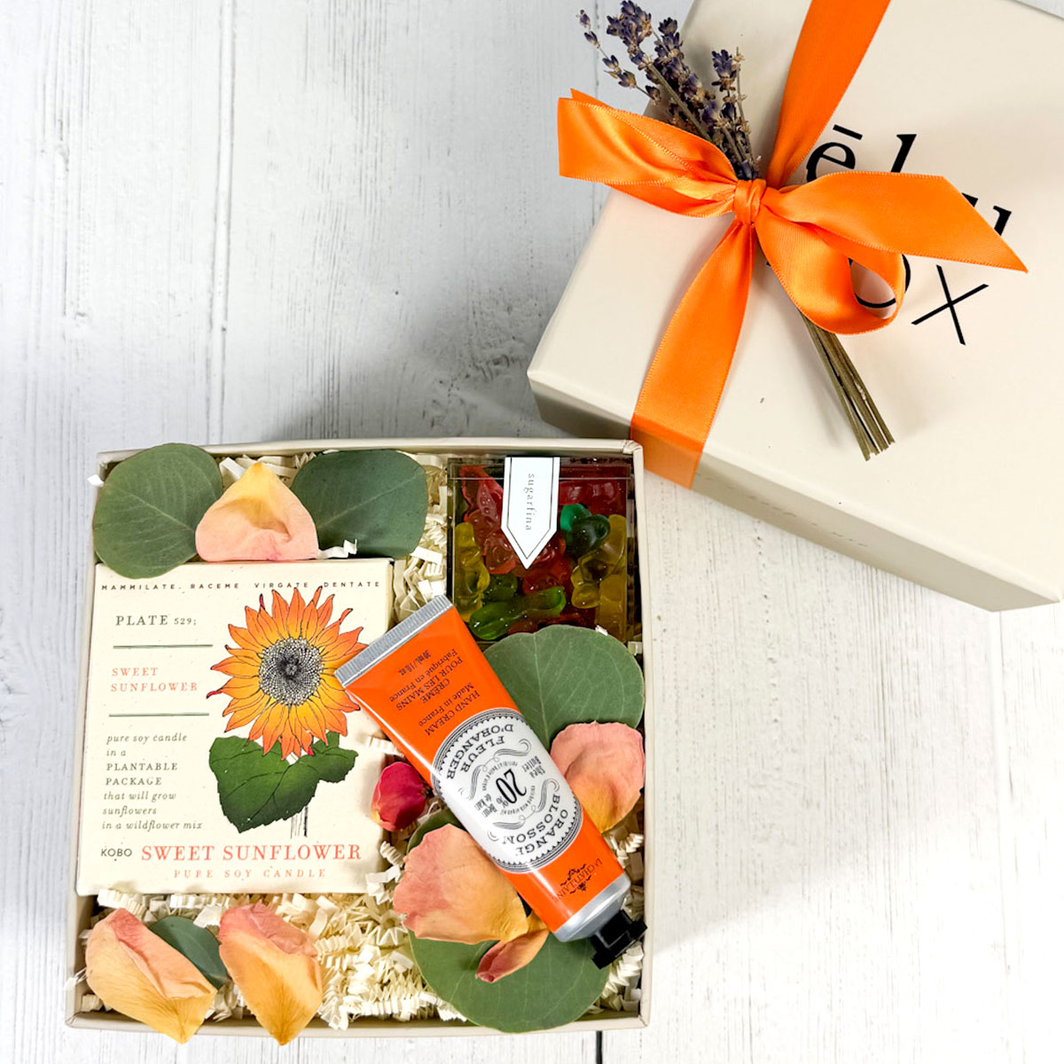 top view of gift box with handcream, candle and candy -gift box with orange ribbon and lavender