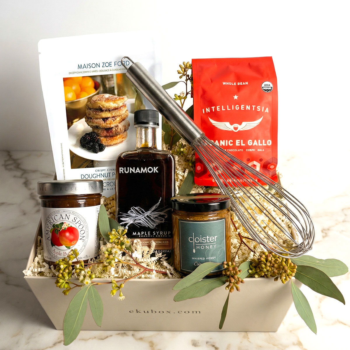 A gourmet breakfast gift box containing a variety of items including pancake mix, runamok maple syrup, cinnamon honey, coffee, a whisk, and preserves.