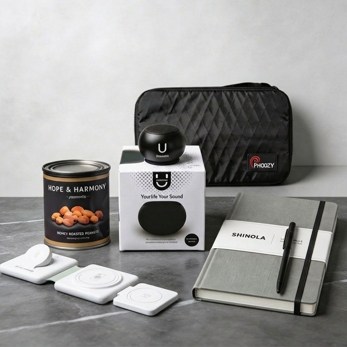 a tech gift displayed on a marble table with a Shinola pen, notebook, a black NASA-tested tech bag, a 3 way charger, a mini speaker and a can of roasted peanuts.