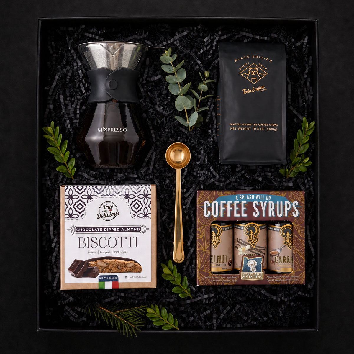 gift box with drip coffee maker, trio of coffee syrups, bisotti, gold coffee scoop and bag of coffee with holiday greens