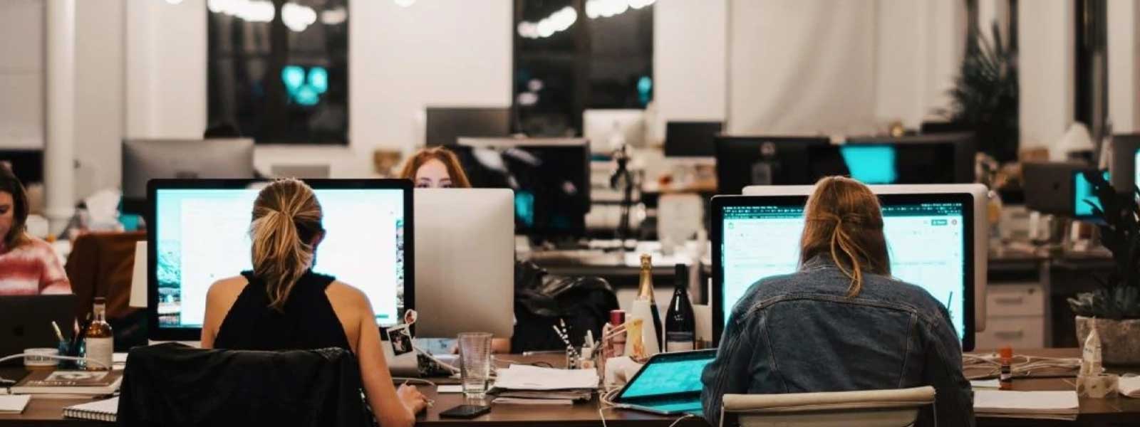 Employees working at computers in a professional office environment, representing workplace teams and employee recognition.