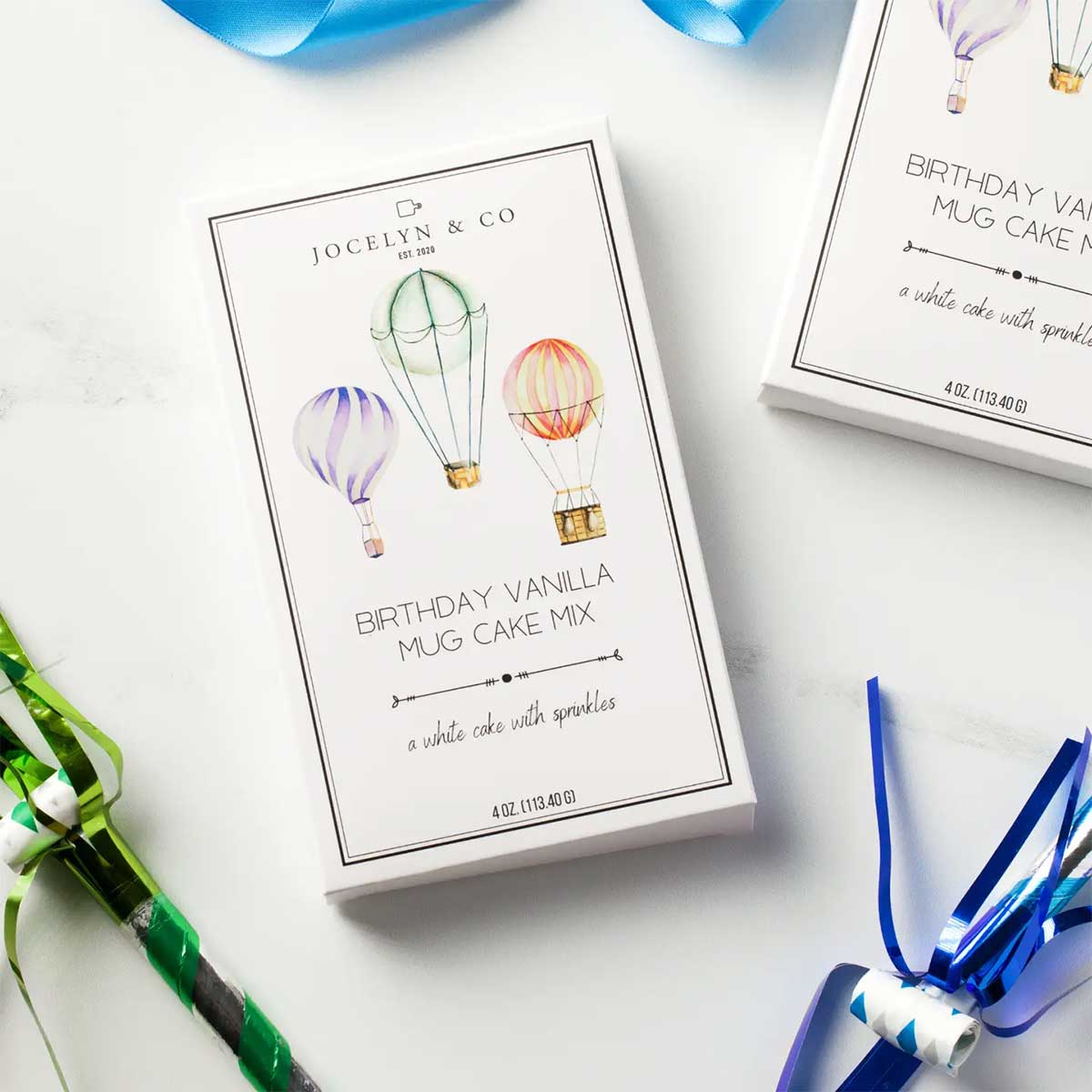 Jocelyn & Co. birthday vanilla mug cake mix packaging on a white surface with colorful ribbons.