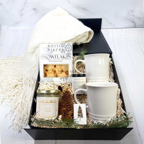 Gift basket with mugs, candles, and a box of cookies on a white surface.