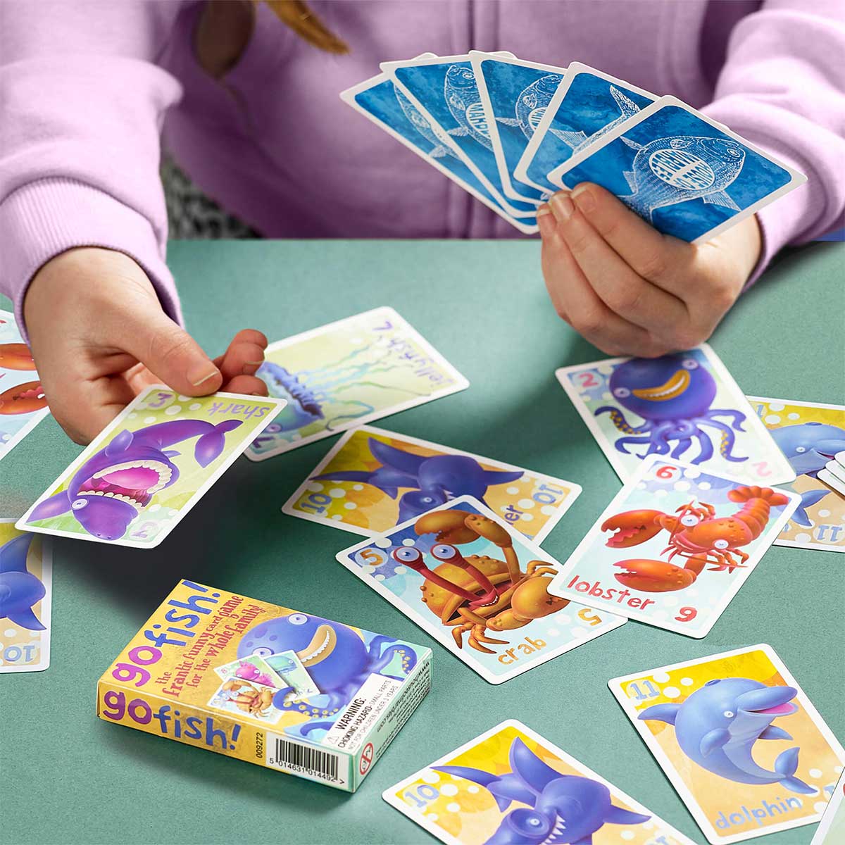 Person playing a card game (Go Fish) with colorful Go Fish cards on a green table