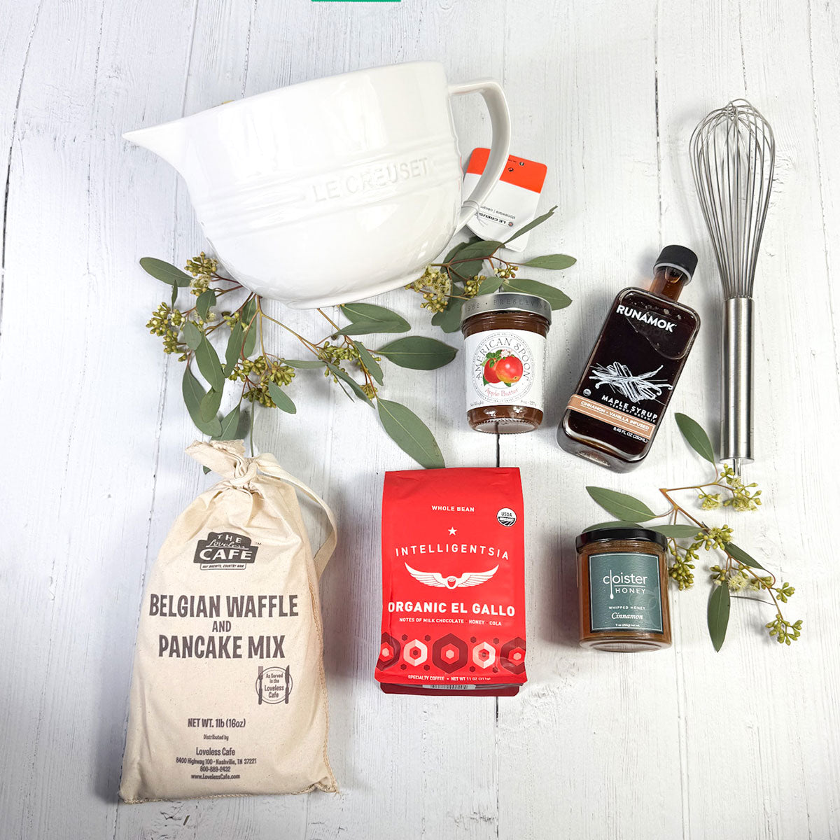 laydown image of the breakfast club gift box with the Le Creuset bow, whisk, pancake mix, coffee, honey, maple syrup and jam.