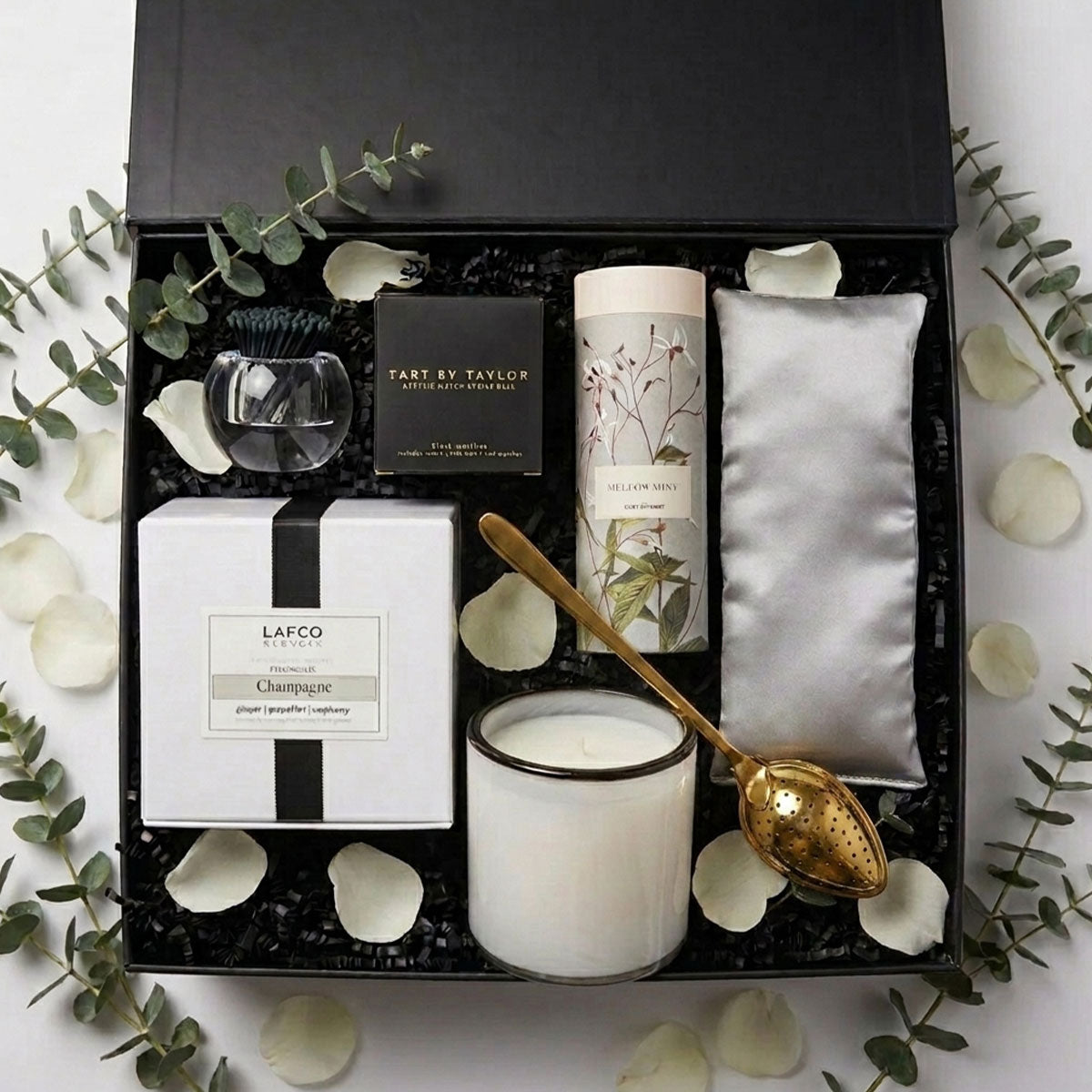 Modern Serenity spa set in a black box with a candle, a tube of tea and a gold spoon, tart by Taylor acrylic match holder and black matches and a silk eye  pillow with rose petals and eucalyptus 