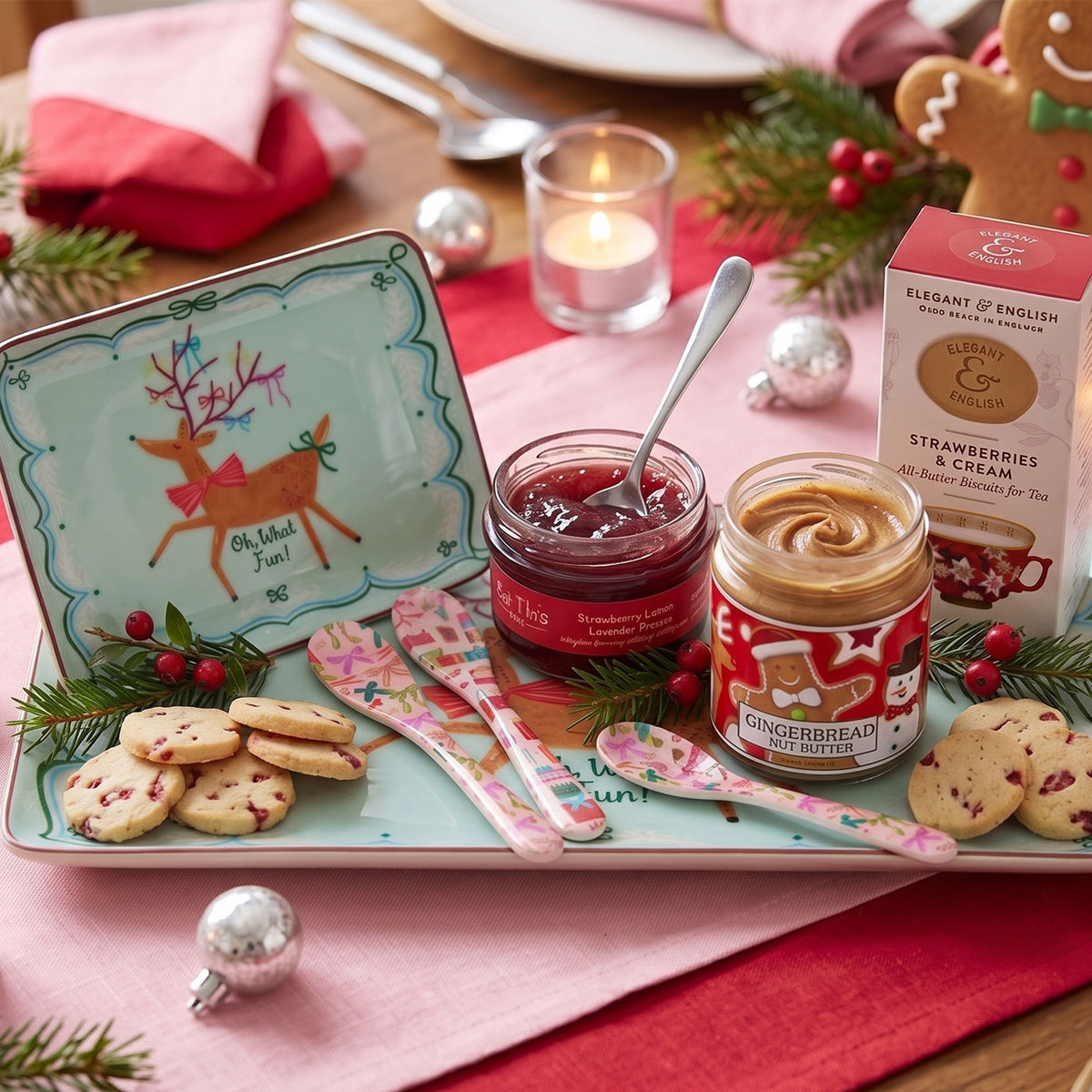 colorful spreader and spoon with a jar of strawberry jam, gingerbread nut butter and a box of strawberry and cream cookies. on a table with pink and red fabric