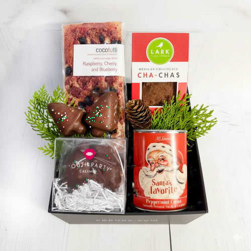 Assorted chocolate treats and a can of peppermint cocoa in a decorative box on a white background