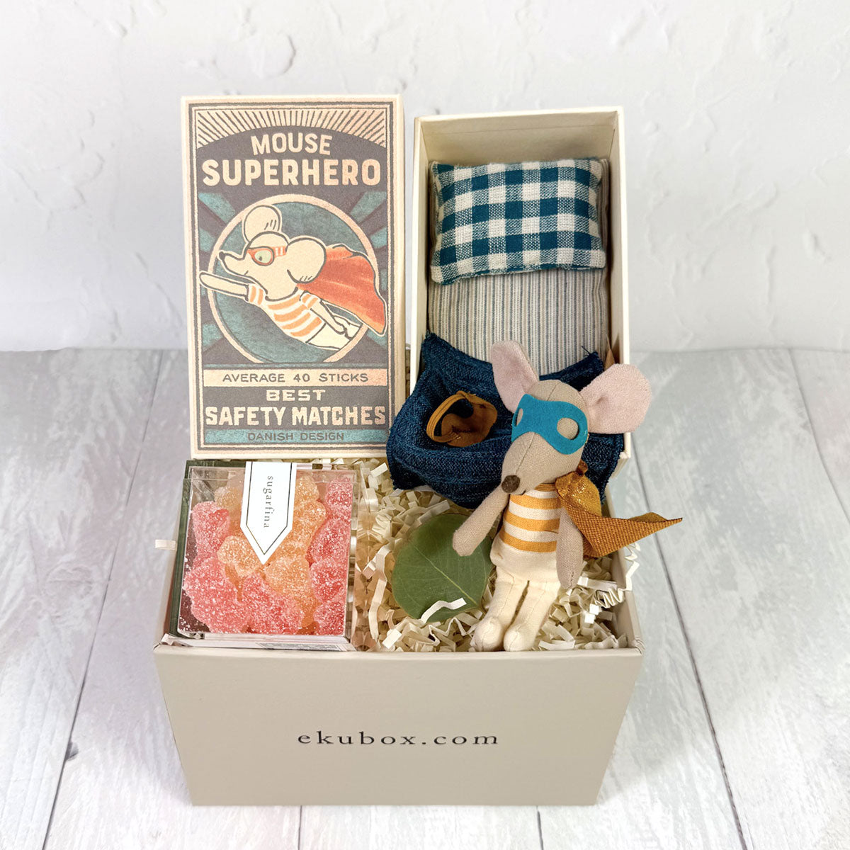 A gift box with a Maileg Superhero Mouse in a matchbox, accompanied by a plush mouse, a gummy treat, and a decorative item.