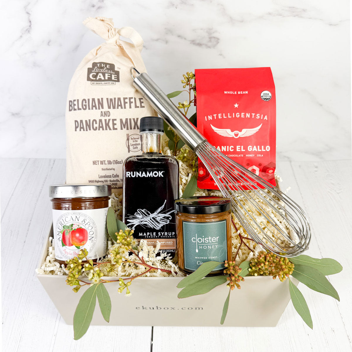 A gourmet breakfast gift box containing a variety of items including pancake mix, runamok maple syrup, cinnamon honey, coffee, a whisk, and preserves.