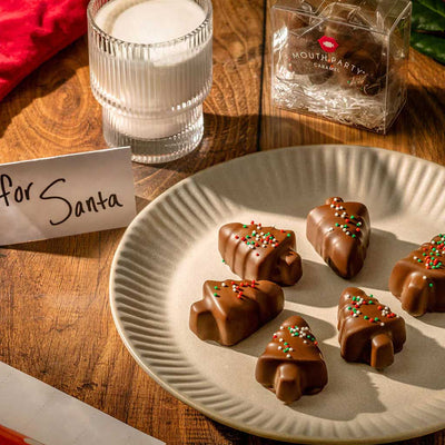 Chocolate tree-shaped chocolate covered caramels on a plate with a glass of milk and a gift box in the background.