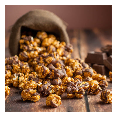 Chocolate-covered popcorn spilling out of a rustic container on a wooden surface.