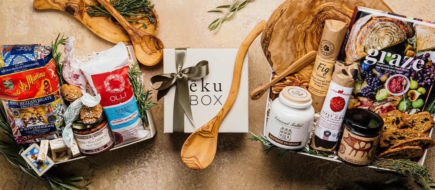 Grazing charcuterie gift box with various snacks, jam, sausage, mustard, cookbook, pasta gift box and a 'Ekuk Box' on a wooden surface.