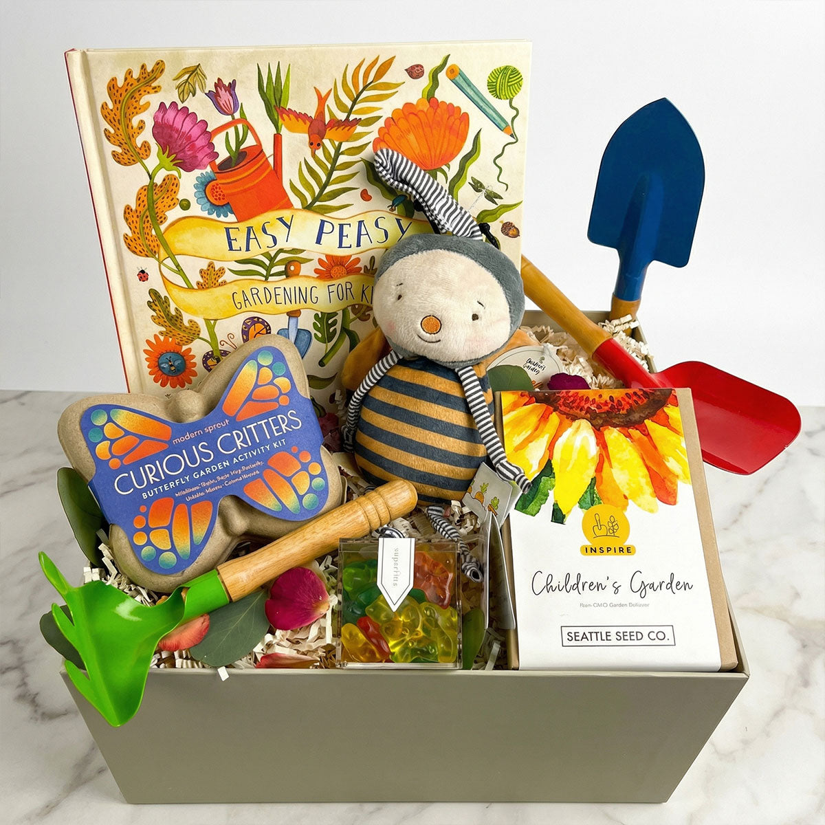 Children's gardening gift set with books Maileg Bee, and tools on a marble surface