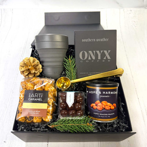Gift basket with coffee, chocolates, popcorn, nuts snacks, and collapsible cups on a white surface