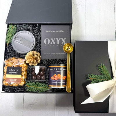 Gift bov with coffee, chocolates, popcorn, nuts snacks, and collapsible cups on a white surface