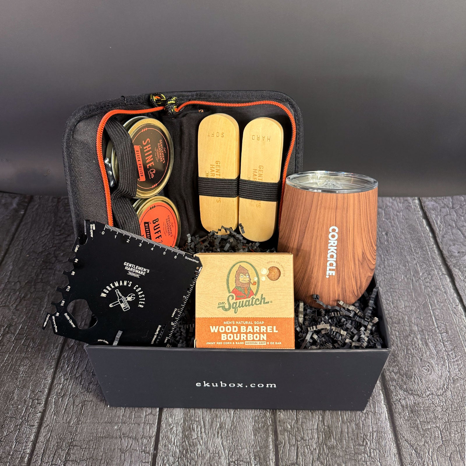 A gift box containing men's grooming essentials including a shoe shine kit, a wood grain stemless cup, and a 20-1 multi-tool coaster, with packaging that reads 'Dapper Dude'.