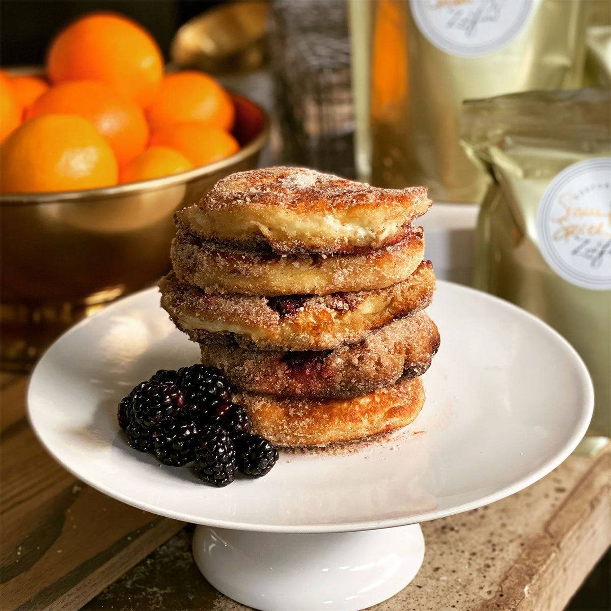 Stack of donut pancakes on a white plate with blackberries, oranges in the background