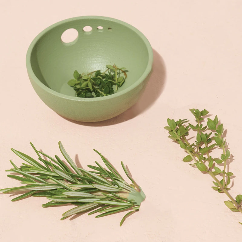 pinch herb bowl with herbs in it and on the side of it on a light pink background